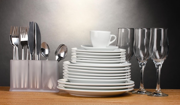 Assiettes propres verres tasse et couverts sur table en bois sur fond gris