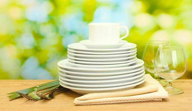 Assiettes propres vides verres et tasse sur table en bois sur fond vert