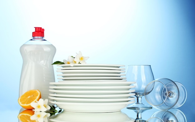 Assiettes et verres propres vides avec du liquide vaisselle et du citron sur fond bleu