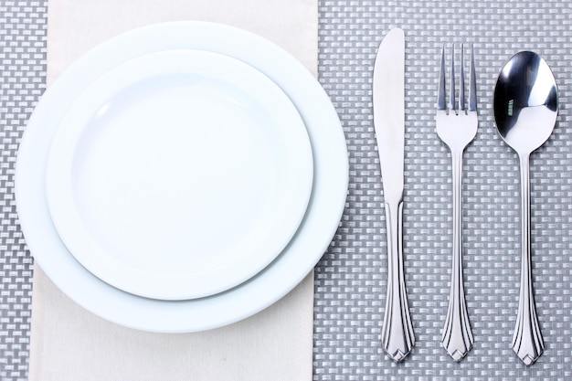 Assiettes vides blanches avec cuillère à fourchette et couteau sur une nappe grise