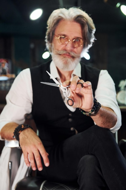 Assis sur la chaise dans le salon de coiffure Un homme senior moderne et élégant aux cheveux gris et à la barbe est à l'intérieur