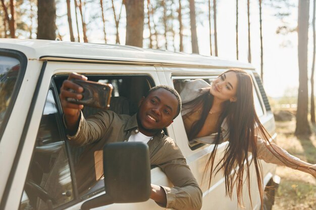 Assis dans la voiture, un jeune couple voyage ensemble dans la forêt pendant la journée