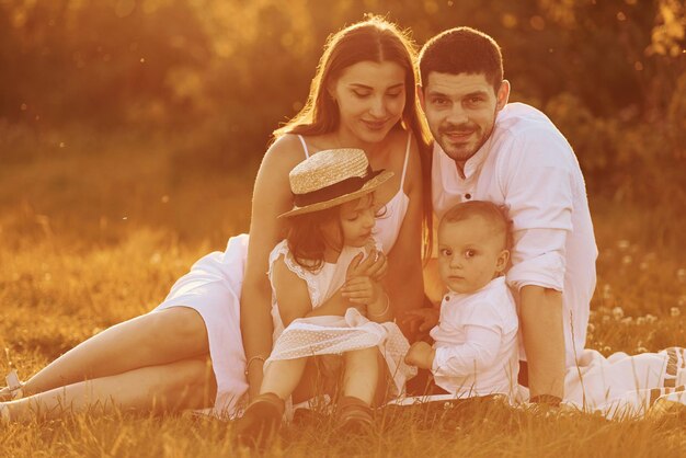 Assis sur l'herbe Père mère avec fille et fils passer du temps libre à l'extérieur à l'heure ensoleillée de l'été