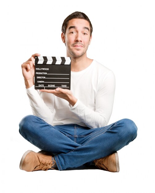 Assis heureux jeune homme en utilisant un clapperboard