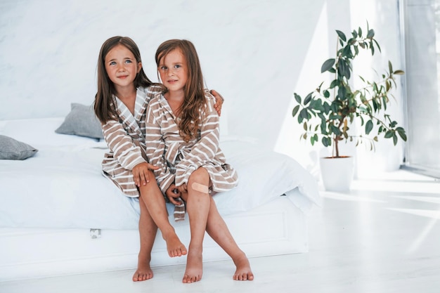 Assis sur le lit Deux mignonnes petites filles à l'intérieur à la maison ensemble