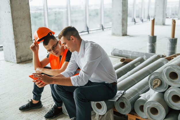 Assis sur les matériaux Homme en costume et bricoleur en vêtements de protection orange travaille sur la construction