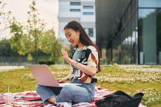 Assis avec un ordinateur portable Jeune femme asiatique est à l'extérieur pendant la journée