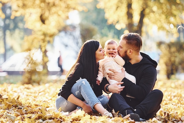 Assis par terre. Joyeuse famille s'amusant avec leur enfant dans un magnifique parc d'automne.