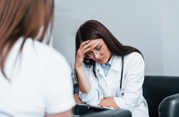 Assis et parler Jeune femme a une visite avec une femme médecin dans une clinique moderne