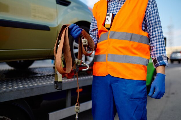 Assistant de dépanneuse mâle tenant des ceintures pour la fixation de la voiture pour le transport en toute sécurité. Photo en gros plan