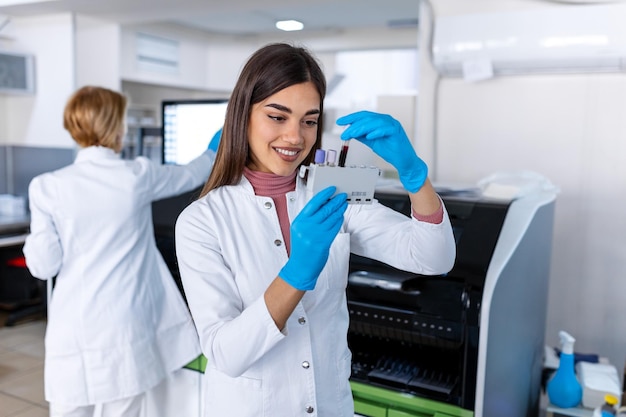 Assistant de laboratoire mettant des tubes à essai dans le support Médecin scientifique regardant un tube à essai sanguin travaillant à une expérience de biochimie dans un laboratoire hospitalier de microbiologie