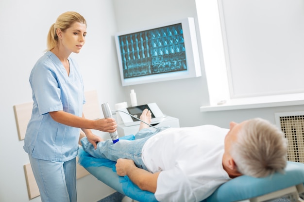 Assistant médical. Agréable belle femme habile debout près du patient et à l'aide d'un appareil à ultrasons lors de l'examen médical