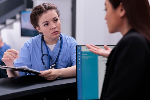 Assistant médical montrant l'expertise du patient à la réceptionniste tout en lui demandant de programmer un autre examen. Personnel médical travaillant dans la zone d'attente de l'hôpital, soutien aux services de soins de santé