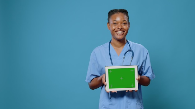 Assistant médical montrant une tablette avec un écran vert horizontal à la caméra. Infirmière avec dispositif de maintien d'uniforme et de stéthoscope avec modèle de maquette isolé et incrustation de chrominance à l'écran.