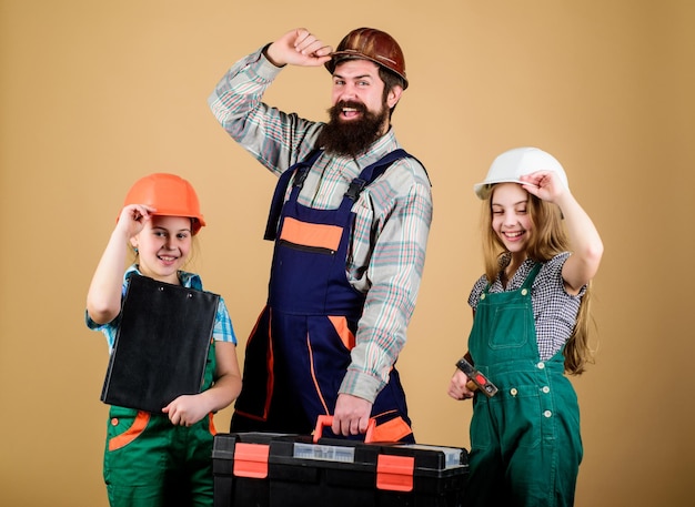 Assistant ouvrier du bâtiment Constructeur ou charpentier Réparateur en uniforme Ingénieur Homme barbu avec des petites filles Réparation Créativité pour enfants Père et fille dans l'atelier Confiance en la sécurité