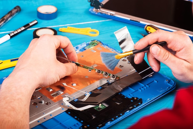 L'assistant répare un ordinateur portable avec des outils et des mains sur la vue de dessus de table en bois bleu