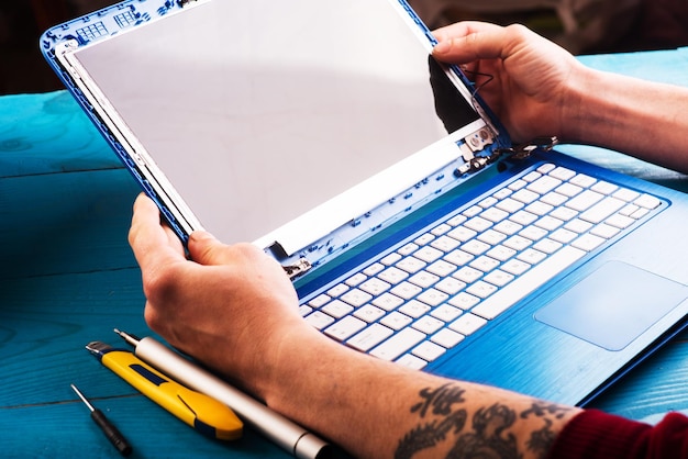 L'assistant répare un ordinateur portable avec des outils et des mains sur la vue de dessus de table en bois bleu