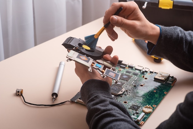 L'assistant répare l'ordinateur portable avec des outils et des mains