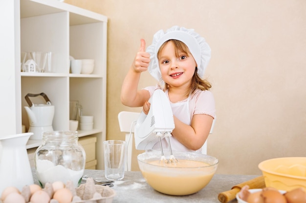 Une assistante joyeuse de jeunes mères pétrit la pâte pour une tarte avec un mélangeur