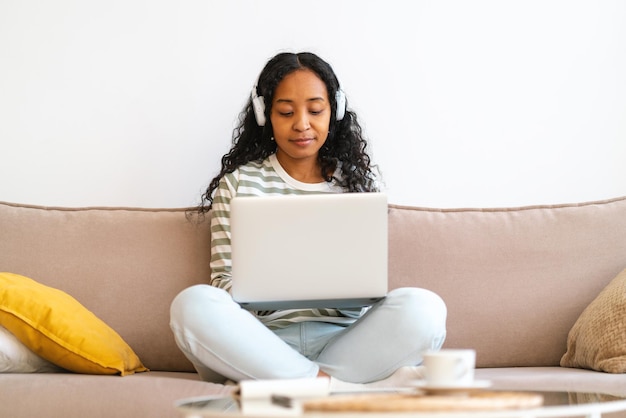 Assister à un cours en ligne à domicile étudiant afro-américain travaillant sur un ordinateur portable en écoutant une conférence