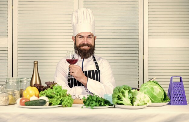 Associez le vin et la nourriture comme un expert L'homme porte un chapeau et un tablier savourez une boisson gustative Le chef cuisinier tient un verre de vin Ajoutez un peu d'alcool Quel vin servir avec le dîner Concept de dîner exquis Dégustation de vin