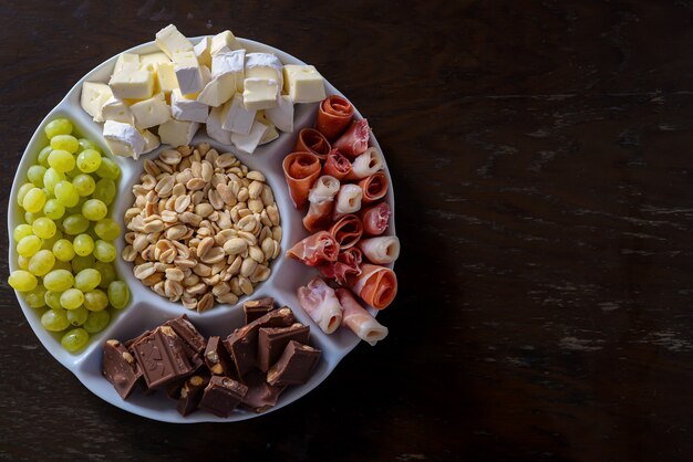 assortiment d'apéritif sur une assiette prise d'au-dessus de noix de bacon fromage chocolat raisins sur un b en bois