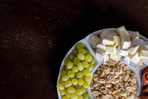 assortiment d'apéritif sur une assiette prise d'au-dessus de noix de bacon fromage chocolat raisins sur un b en bois