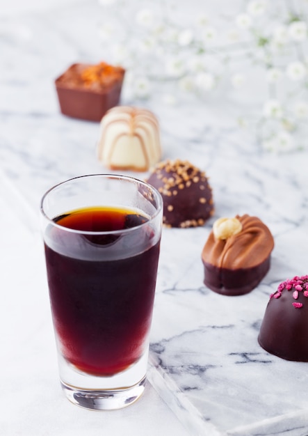 Assortiment de bonbons de luxe au chocolat blanc et noir sur fond de marbre blanc avec verre de liqueur botanique