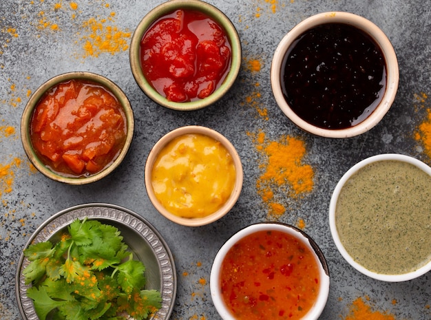 Assortiment de chutneys indiens dans de petits bols rustiques sur fond de béton gris. Vue de dessus du chutney coloré, des sauces indiennes traditionnelles et des trempettes comme collation ou plat d'accompagnement, gros plan