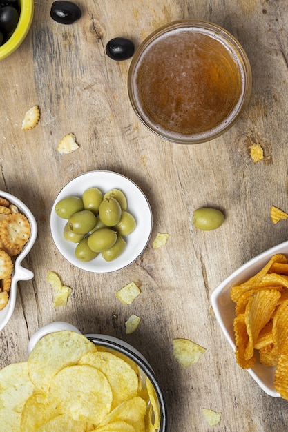 Assortiment de collations à la maison avec croustilles, bière, craquelins, olives vertes et noires sur table en bois