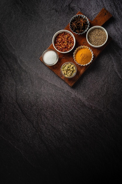 Assortiment de condiments à plat avec planche de bois sur fond sombre