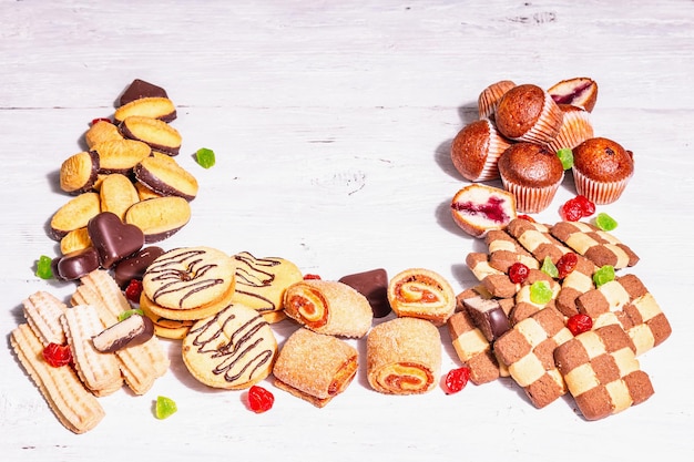 Assortiment de divers biscuits et cupcakes. Lumière dure à la mode, ombre sombre. Fond de planches de bois blanc, espace de copie