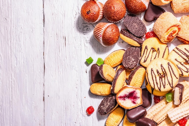 Assortiment de divers biscuits et cupcakes. Lumière dure à la mode, ombre sombre. Fond de planches de bois blanc, vue de dessus