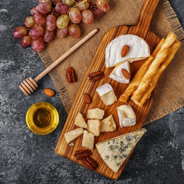 Assortiment de fromage avec du miel, des noix et du raisin sur une planche à découper