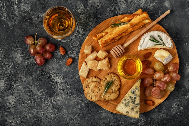 Assortiment de fromage avec du vin, du miel, des noix et du raisin sur une planche à découper