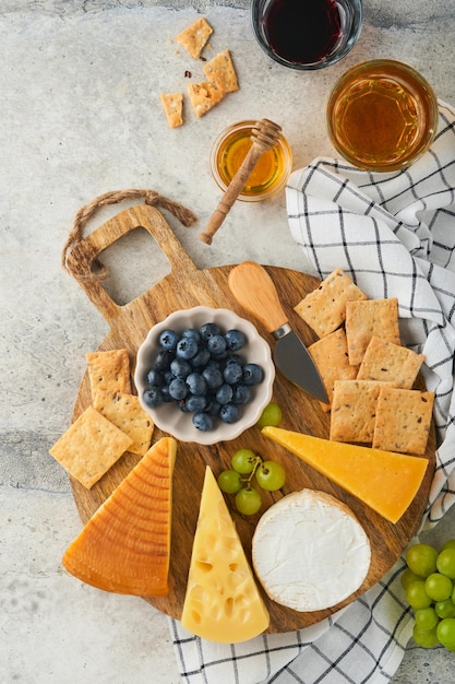 Assortiment de fromage miel cracker myrtilles raisins avec du vin rouge et blanc dans des verres serveur d'antipasti sur planche de marbre blanc sur fond gris Assiette de fromage Espace de copie plat