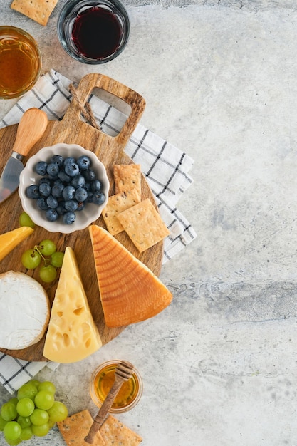 Assortiment de fromage miel cracker myrtilles raisins avec du vin rouge et blanc dans des verres serveur d'antipasti sur planche de marbre blanc sur fond gris Assiette de fromage Espace de copie plat