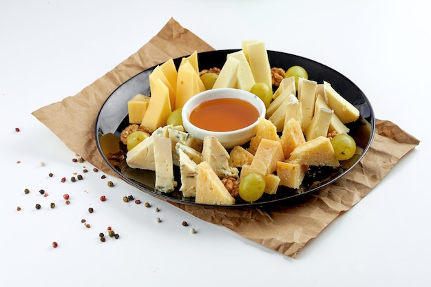 Assortiment de fromages alléchants: dorblu, parmesan, fromages à pâte molle, servis dans une assiette noire avec raisins et miel