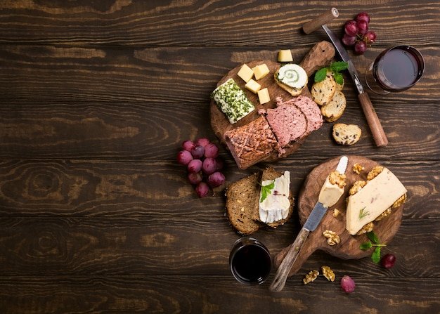 Assortiment de fromages sur une assiette en bois, raisins, pain, vin et pâté