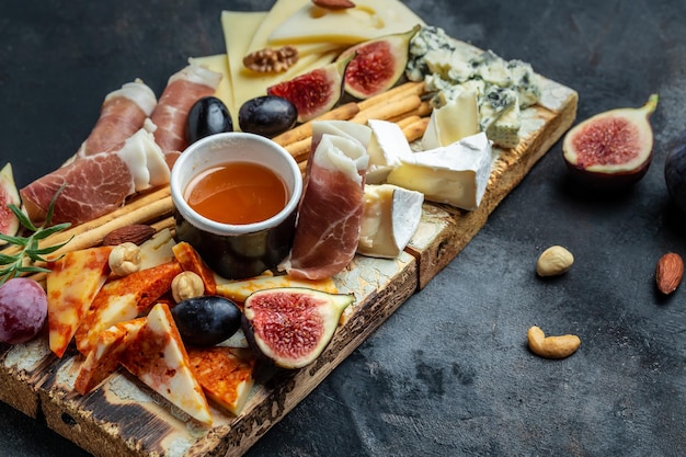 Assortiment de fromages au prosciutto miel noix et raisin sur planche à découper Plateau de fromages