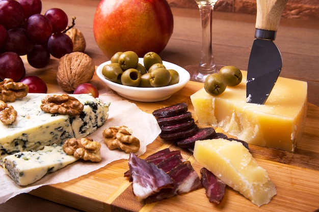 Assortiment de fromages aux fruits, raisins, noix, verre à vin et couteau à fromage sur un plateau de service en bois