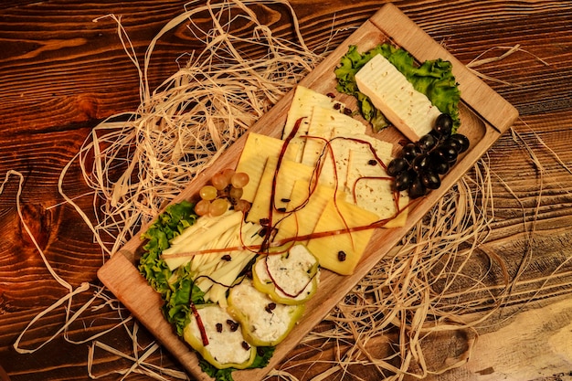 Assortiment de fromages dans un plateau en bois avec des raisins décorés d'herbe séchée