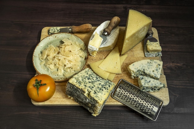 Assortiment de fromages nature morte avec des couteaux tomate fromage bleu parmesan flocons et grattoirs sur planche de bois