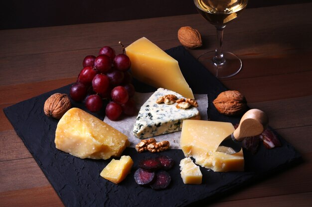 Assortiment de fromages, noix, raisins, viande fumée et verre de vin.