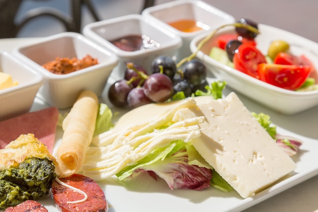 Assortiment de fromages avec des raisins, des tomates, des concombres et des sauces.