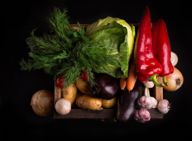 Assortiment de légumes crus frais dans une boîte en bois sur fond noir. Nourriture locale biologique.