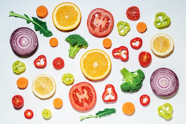 Assortiment de légumes et de fruits en tranches sur une surface blanche.