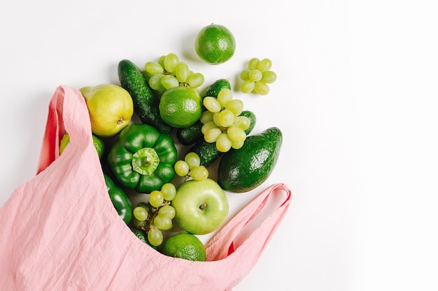 Assortiment de légumes verts frais biologiques crus dans un sac en coton écologique rose, pose à plat, vue de dessus