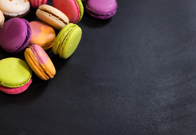 Assortiment de macarons biscuits français colorés sur fond noir.