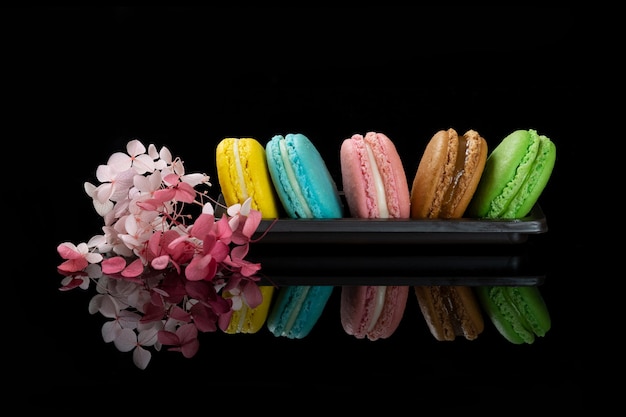 Un assortiment de macarons sur fond noir avec de beaux reflets.